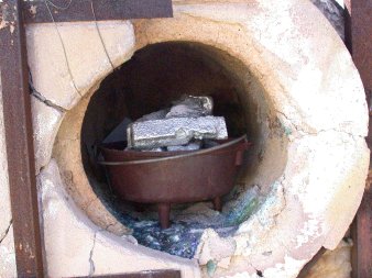 Glory hole loaded with cooking pot with aluminum ingots and ceramic behind, sand below.